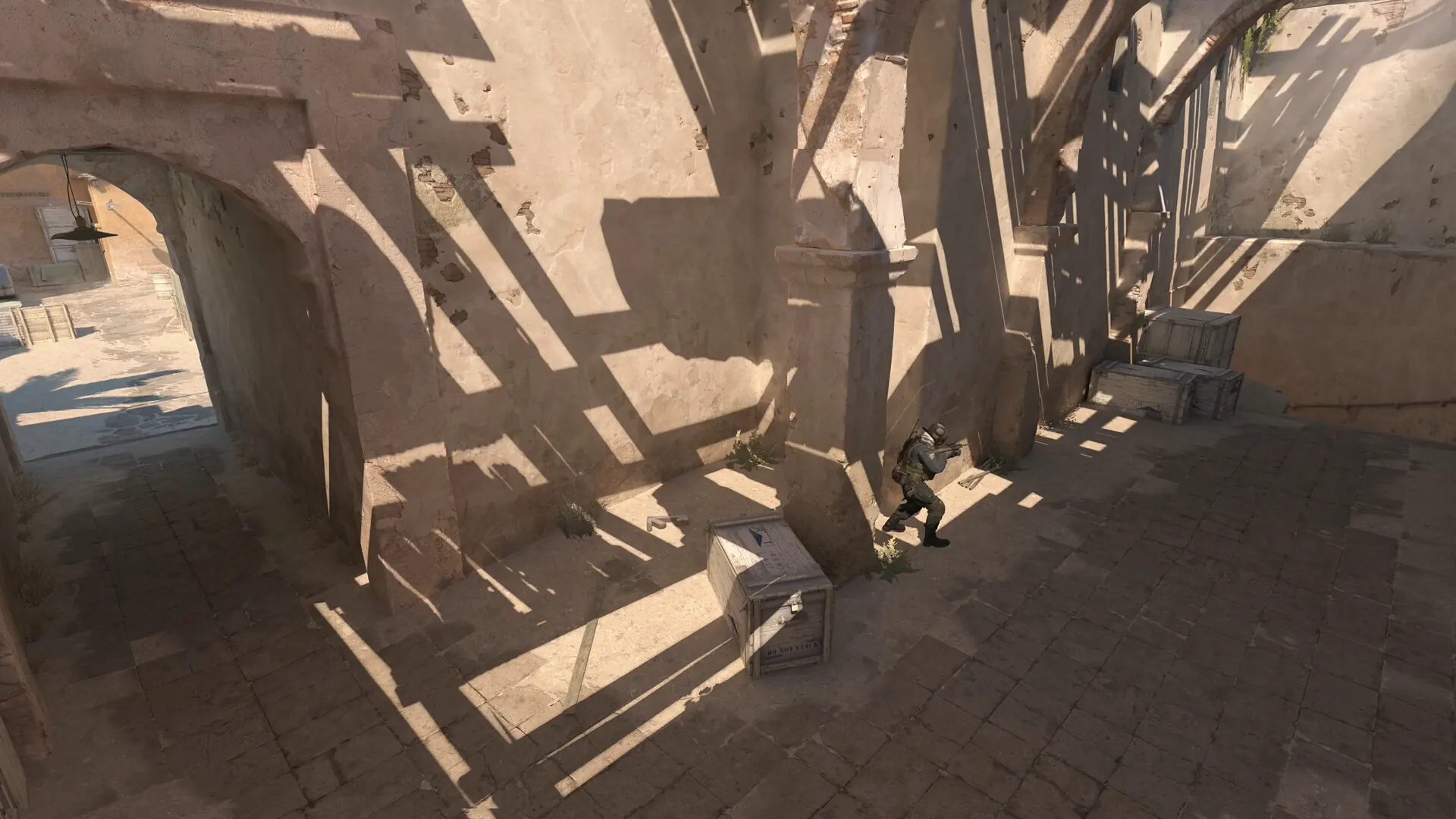 Official CS2 store screenshot showing a player near stone cover with an open courtyard route